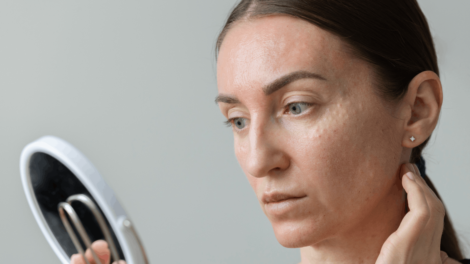 woman looking into mirror examining her skin 