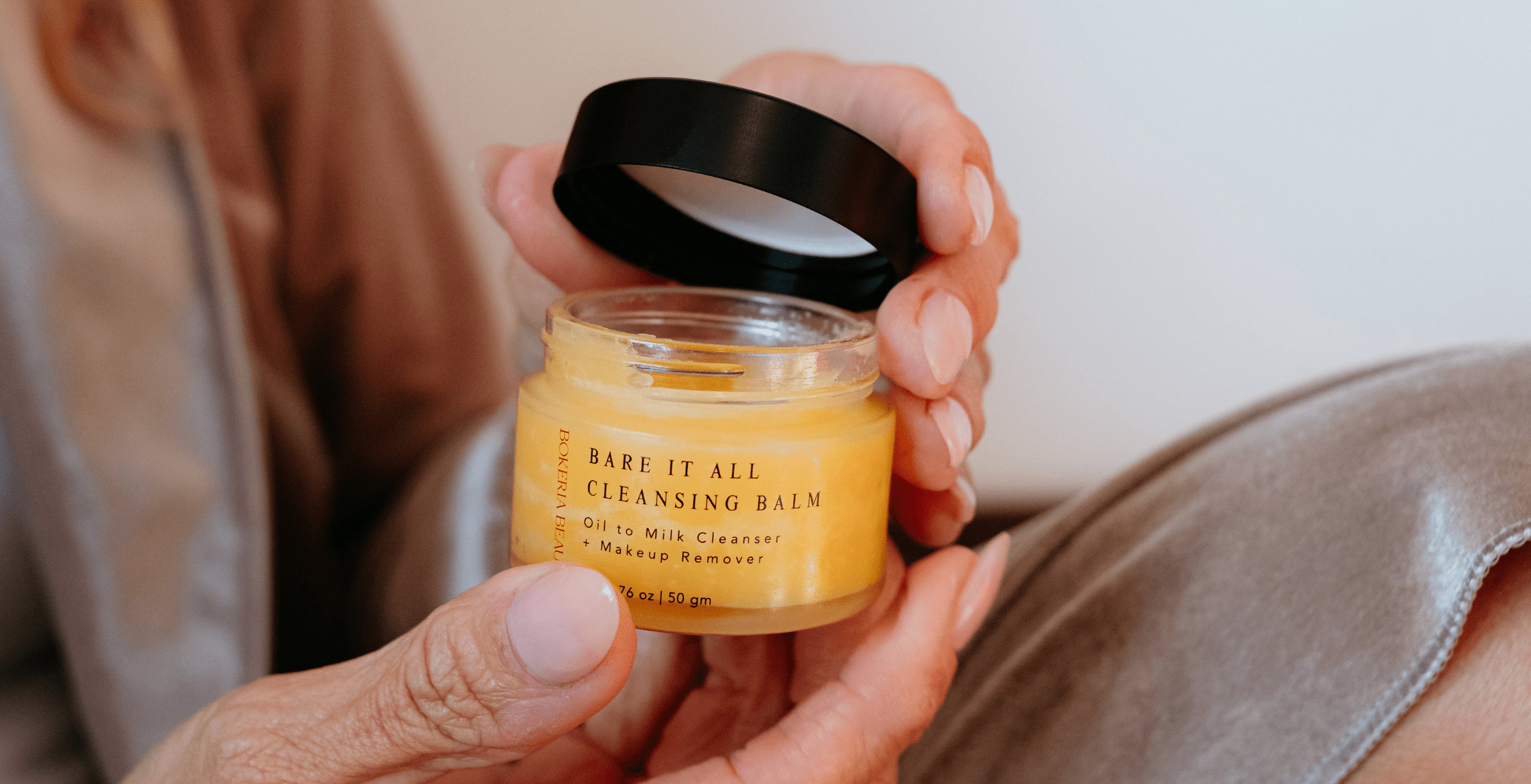 Person holding a jar of 'Bare It All' cleansing balm with a neutral background