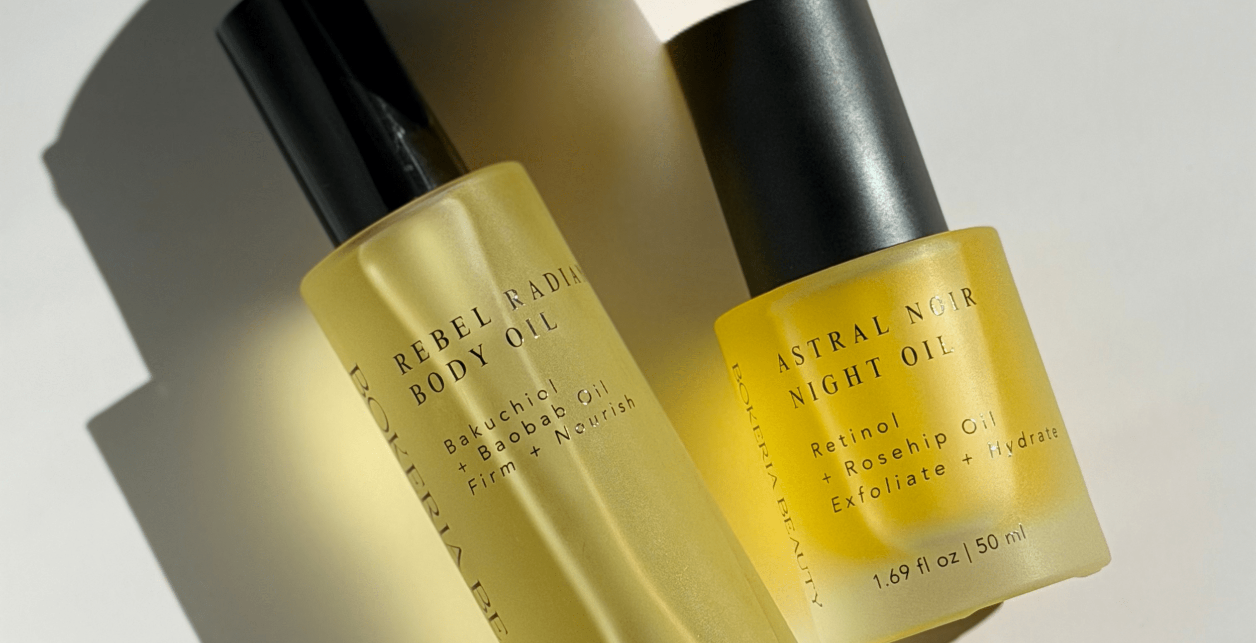 Two yellow bottles of Rebel Radiance Body and Astral Noir body oils on a light background