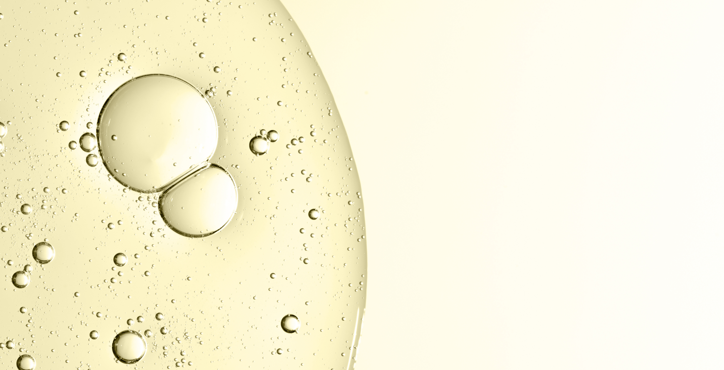 Close-up of oil droplets on a clear liquid surface with a light yellow background